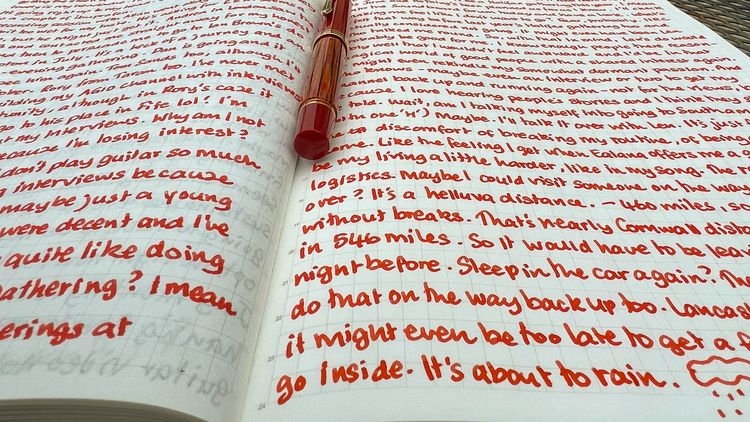 Notebook with two pages of handwriting and a fountain pen in the crease of the pages. 